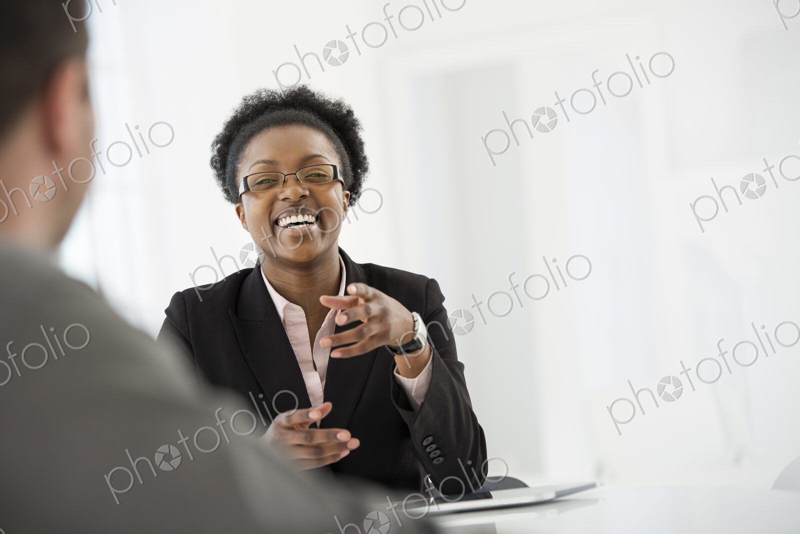 A fresh white building interior, flooded with light. A woman in a black suit jacket…