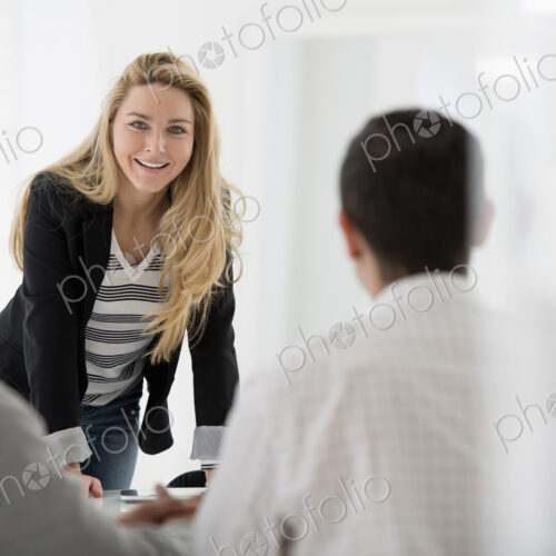 A fresh white building interior, flooded with light. A woman leaning on a tabletop…