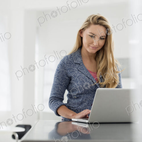A fresh white building interior, flooded with light. A woman sitting at a table using… A fresh white building interior, flooded with light. A woman sitting at a table using…