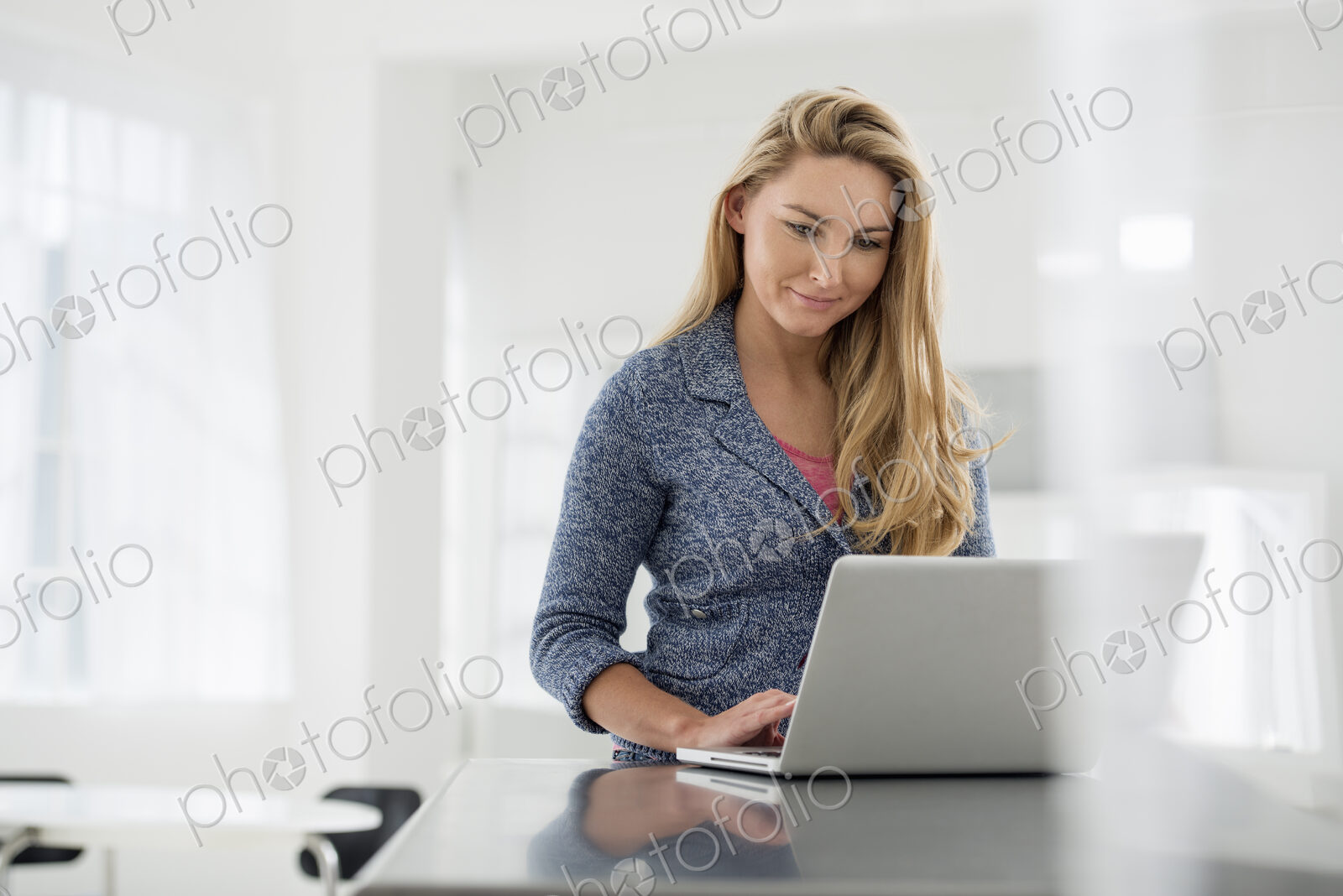 A fresh white building interior, flooded with light. A woman sitting at a table using…