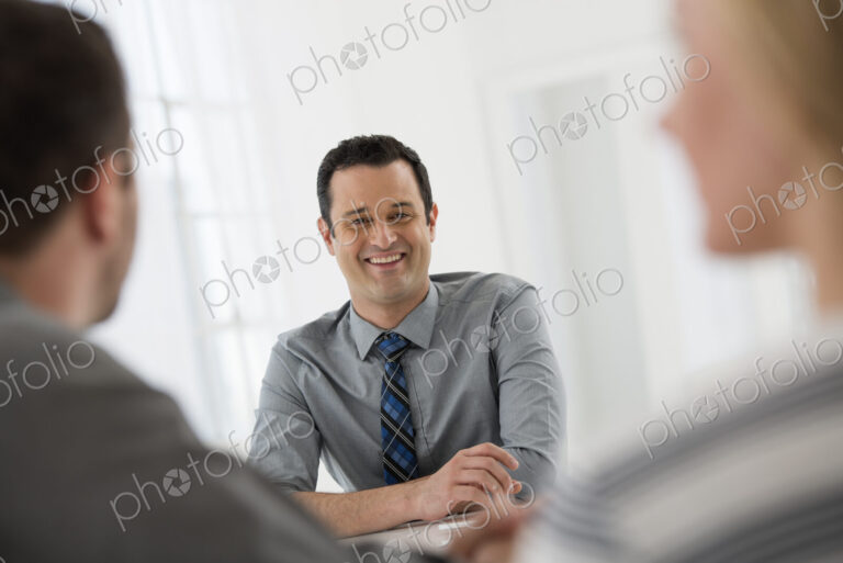 A fresh white building interior, flooded with light. Three people sitting around a…