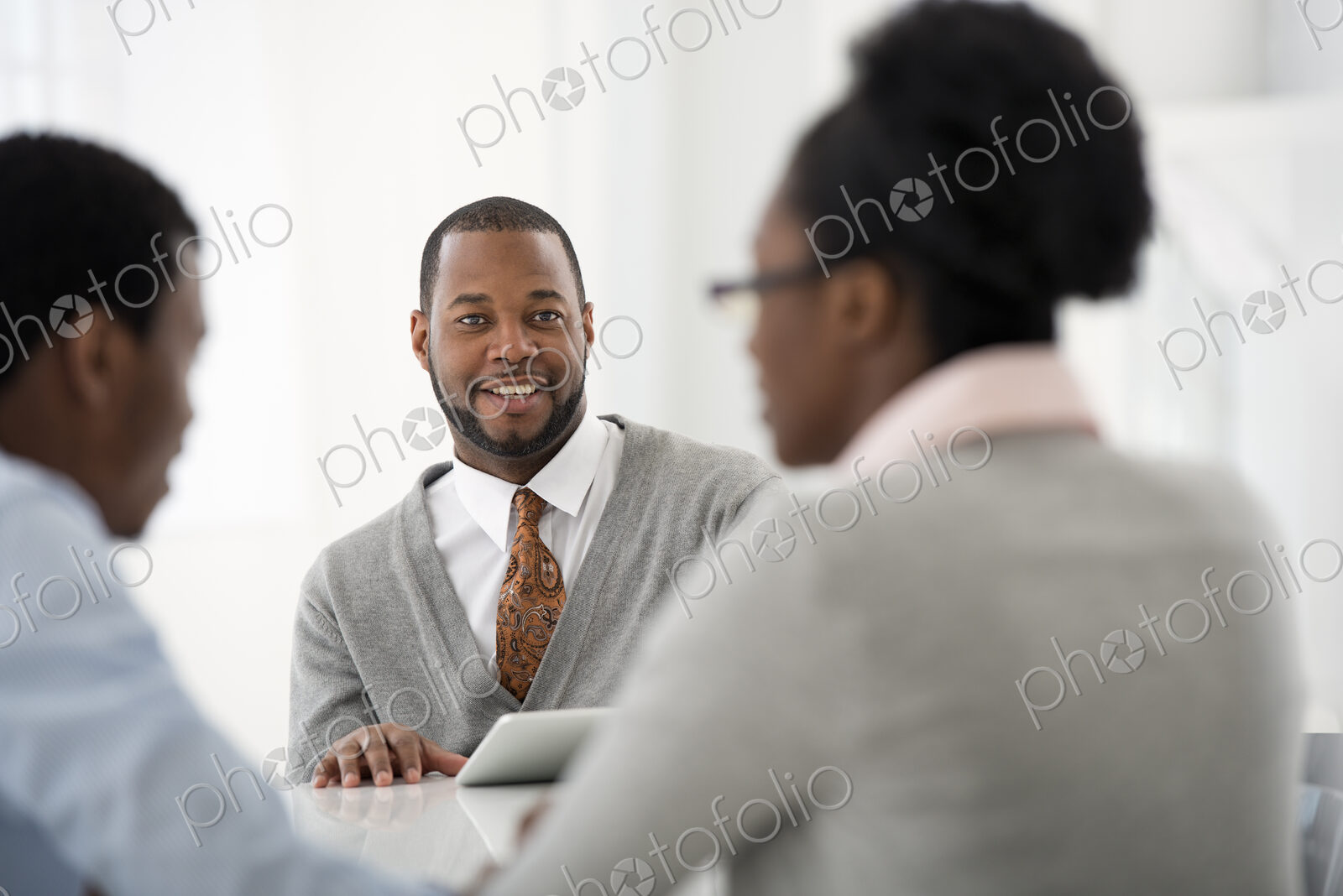 A fresh white building interior, flooded with light. Three people sitting around a…