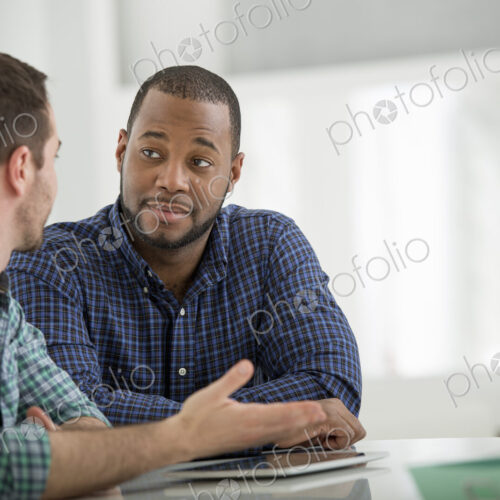 A fresh white building interior, flooded with light. Two men sitting at a table and…