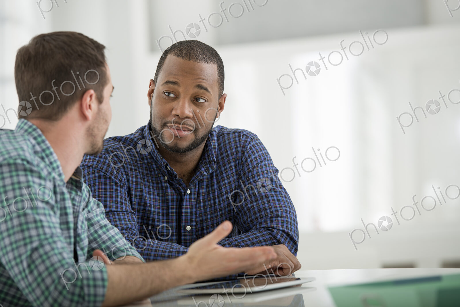 A fresh white building interior, flooded with light. Two men sitting at a table and…