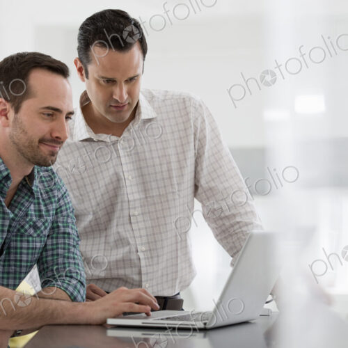 A fresh white building interior, flooded with light. Two men standing at a table using…