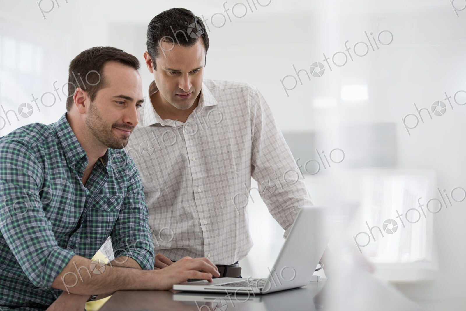 A fresh white building interior, flooded with light. Two men standing at a table using…