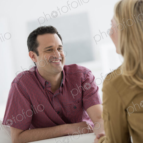 A fresh white building interior, flooded with light. Two people talking to each other,…