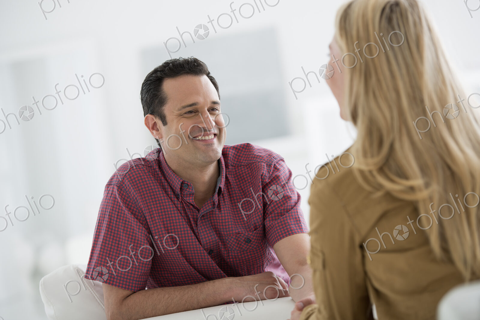 A fresh white building interior, flooded with light. Two people talking to each other,…