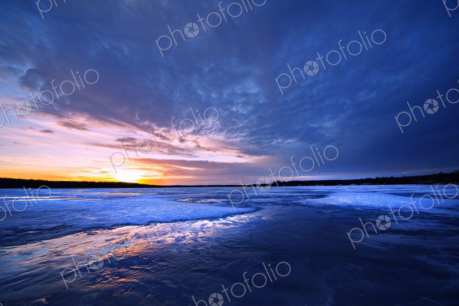 A frozen lake at dusk, and view to the setting sun on the horizon.