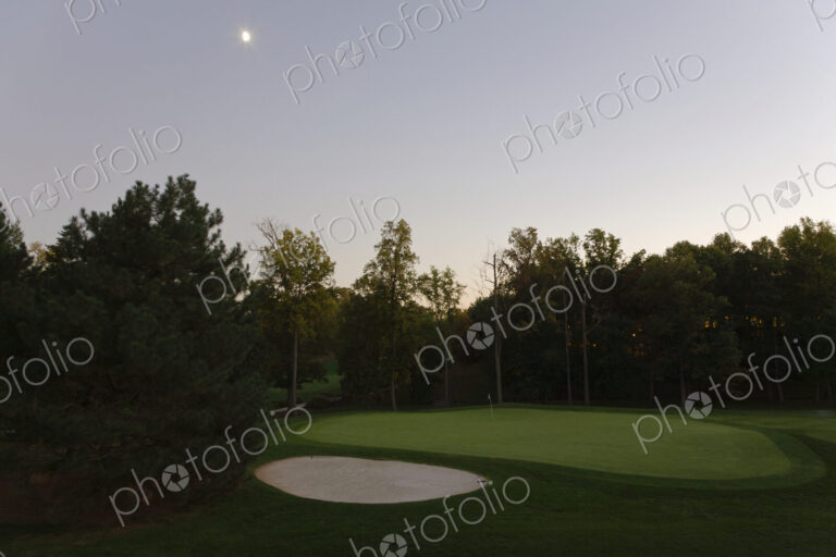 A full moon in the sky at dusk, hanging over a sand trap on a golf course.