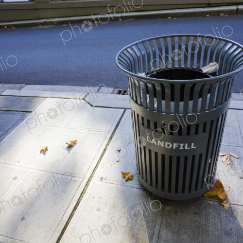 A garbage can on the sidewalk in the city.