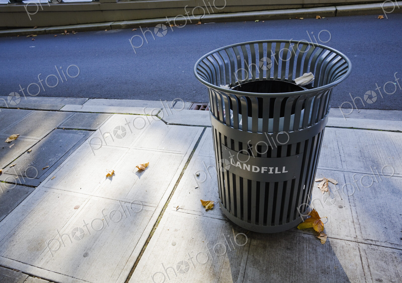 A garbage can on the sidewalk in the city.