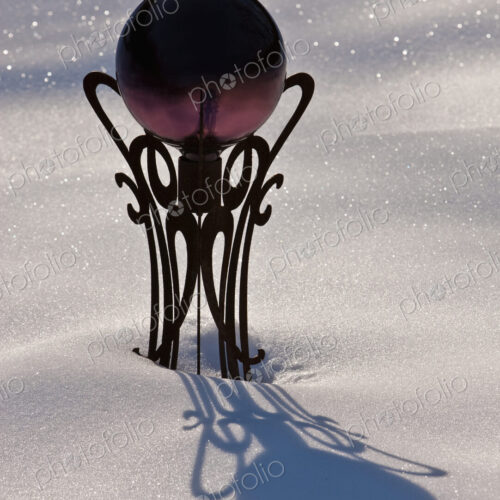 A garden viewing ball on its pedestal in sparkling snow.