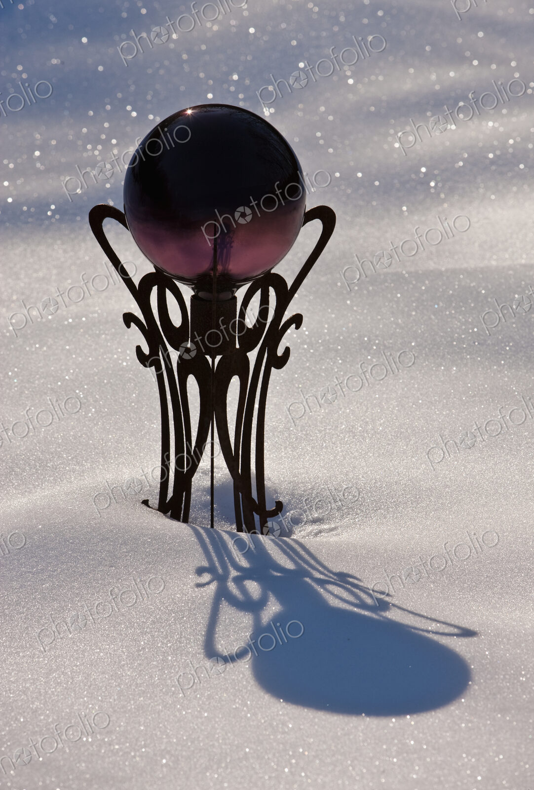 A garden viewing ball on its pedestal in sparkling snow.