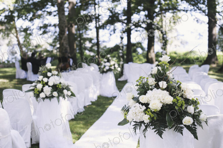 A garden with tables laid under the shade of tall trees, set for a wedding