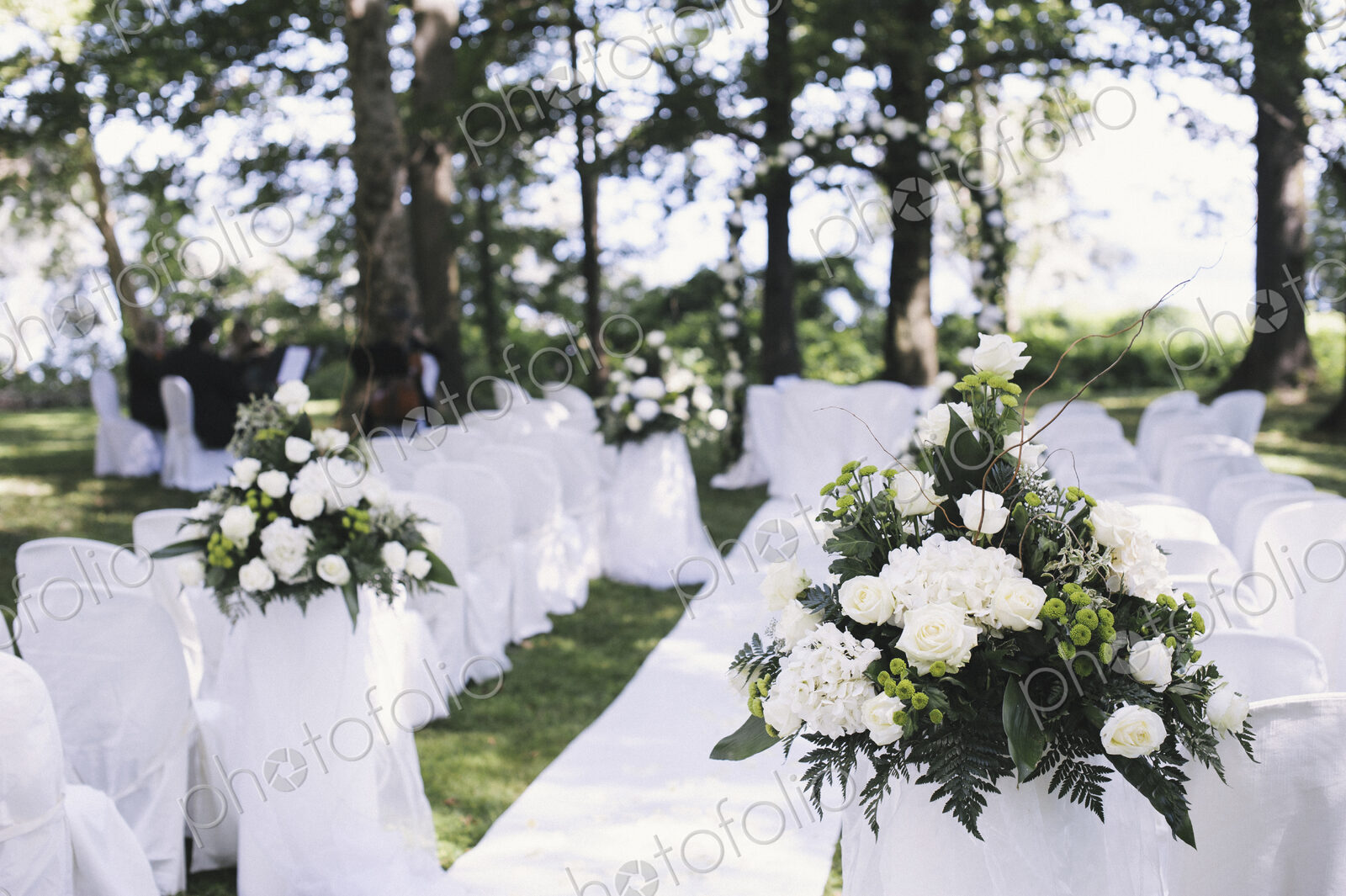 A garden with tables laid under the shade of tall trees, set for a wedding