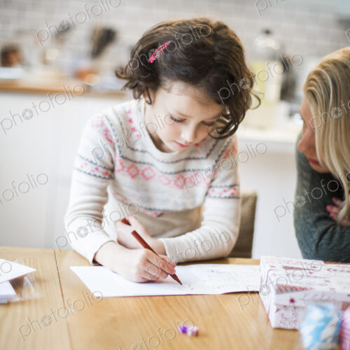 A girl at a table drawing in a card, a letter to Santa.