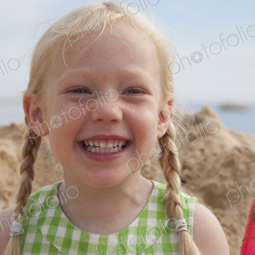 A girl beside a huge pile of sand on the beach, grinning at the camera. A girl beside a huge pile of sand on the beach, grinning at the camera.