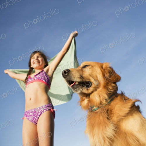 A girl in a beach towel with a golden retriever dog.