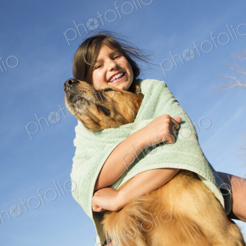 A girl in a beach towel with a golden retriever dog.
