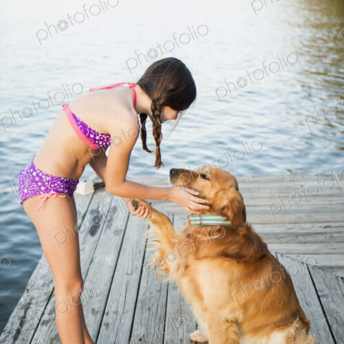 A girl in a bikini with a golden retriever dog lifting its paw up.