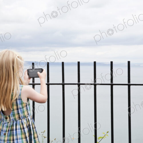 A girl in a checked sundress taking a photograph with a smart phone. A girl in a checked sundress taking a photograph with a smart phone.