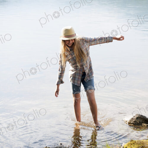 A girl in a straw hat paddling in the shallow waters of a mountain lake. A girl in a straw hat paddling in the shallow waters of a mountain lake.