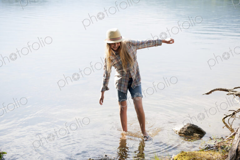 A girl in a straw hat paddling in the shallow waters of a mountain lake.