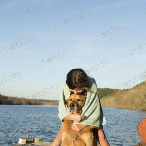 A girl in a swimming towel, cuddling a golden retriever dog.