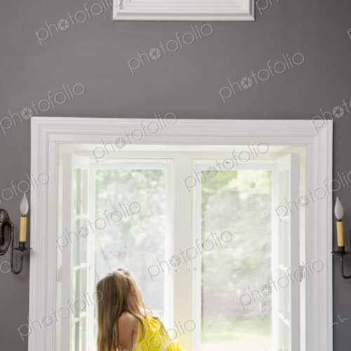 A girl in a white dress seated by a window playing.