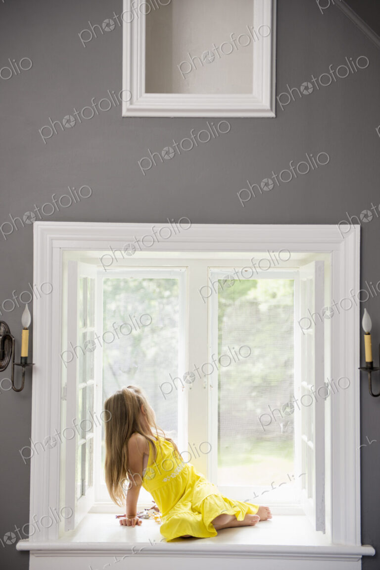 A girl in a white dress seated by a window playing.