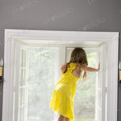 A girl in a white dress seated by a window playing.