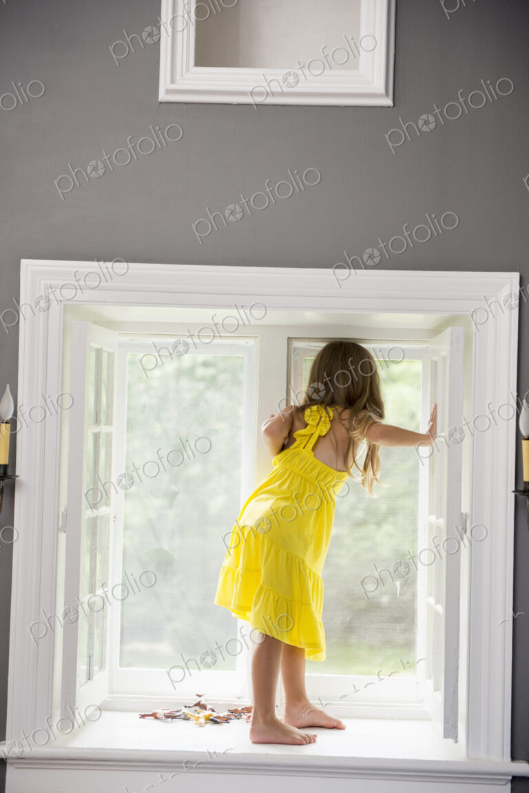 A girl in a white dress seated by a window playing.
