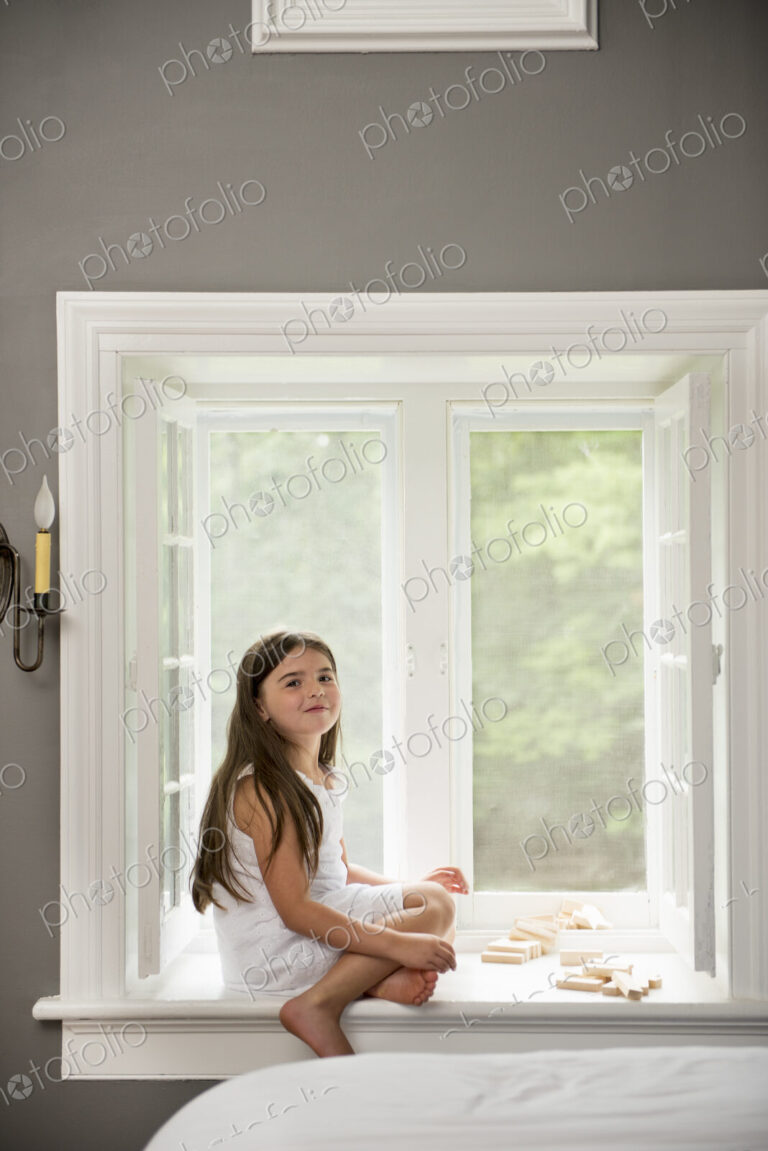 A girl in a white dress seated by a window playing.