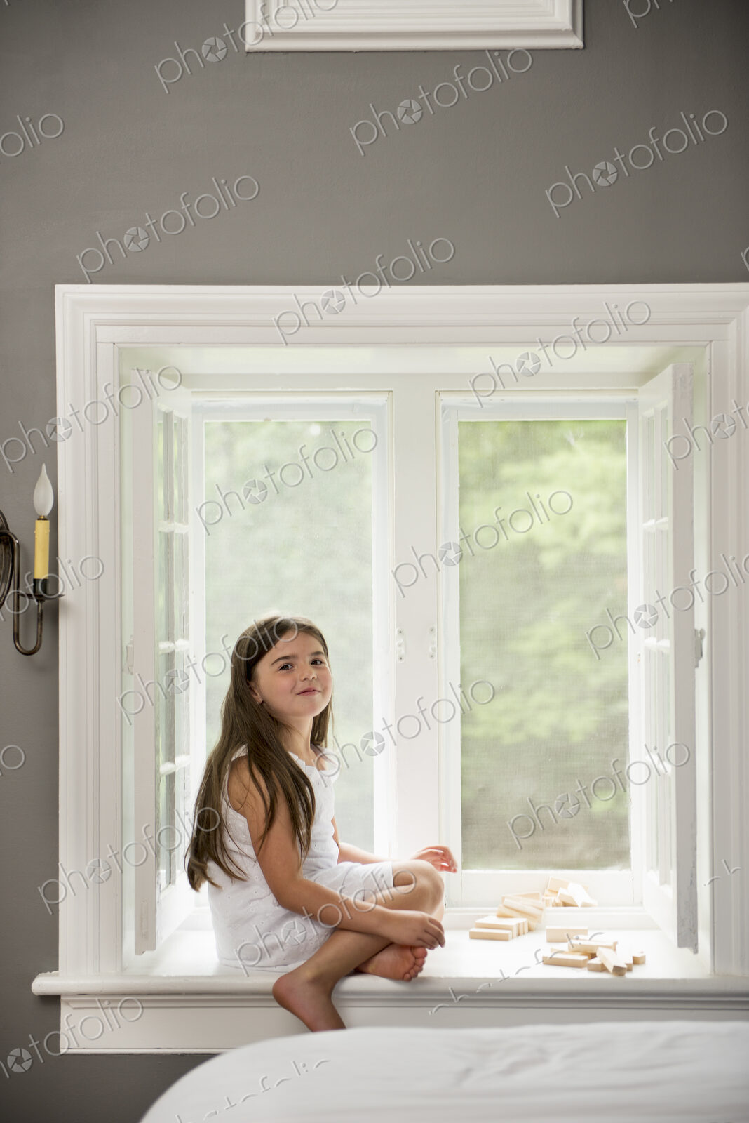 A girl in a white dress seated by a window playing.