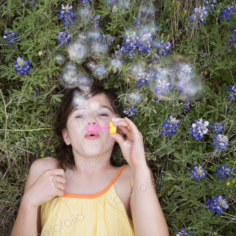A girl lying on her back blowing bubbles in the air.