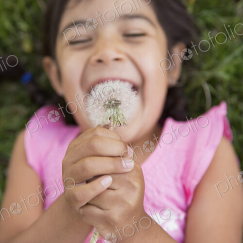 A girl lying on the ground, holding a dandelion seedhead clock. A girl lying on the ground, holding a dandelion seedhead clock.