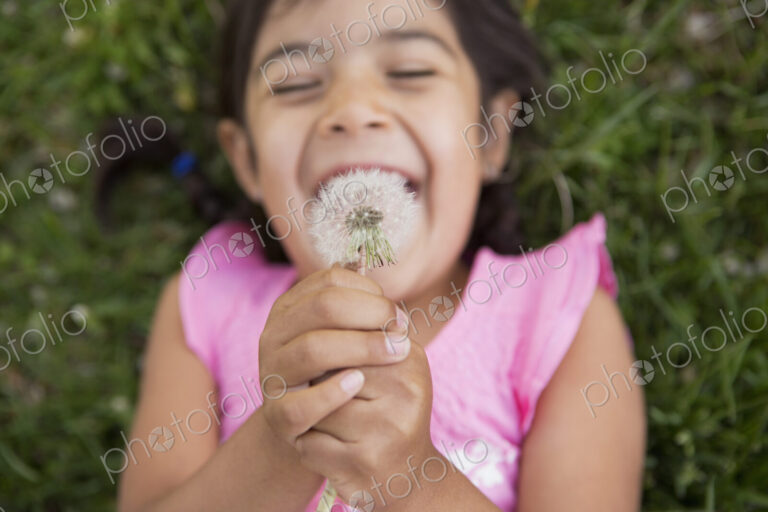 A girl lying on the ground, holding a dandelion seedhead clock.