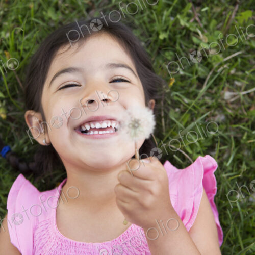 A girl lying on the ground, holding a dandelion seedhead clock. A girl lying on the ground, holding a dandelion seedhead clock.