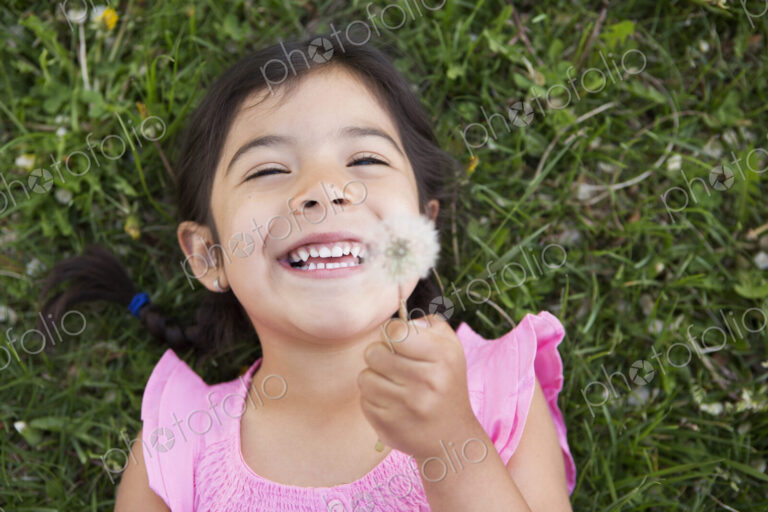 A girl lying on the ground, holding a dandelion seedhead clock.