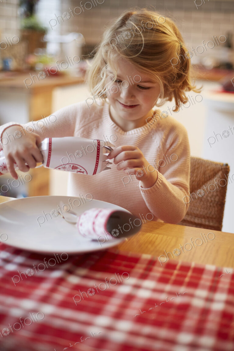 A girl opening a Christmas cracker at a table.