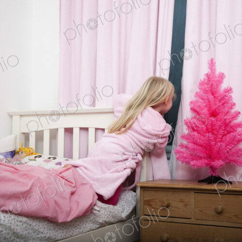 A girl peering through the curtains in her bedroom into the night at Christmas. A girl peering through the curtains in her bedroom into the night at Christmas.