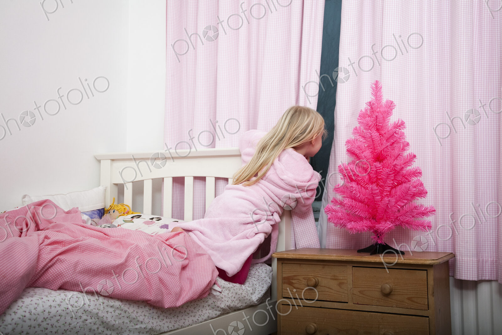 A girl peering through the curtains in her bedroom into the night at Christmas.