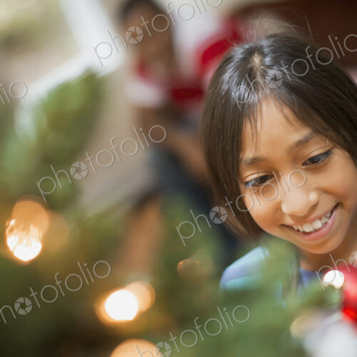 A girl placing a handmade ornament on a Christmas tree. A girl placing a handmade ornament on a Christmas tree.