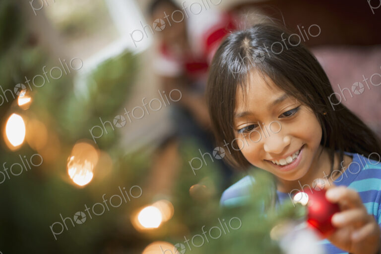 A girl placing a handmade ornament on a Christmas tree.