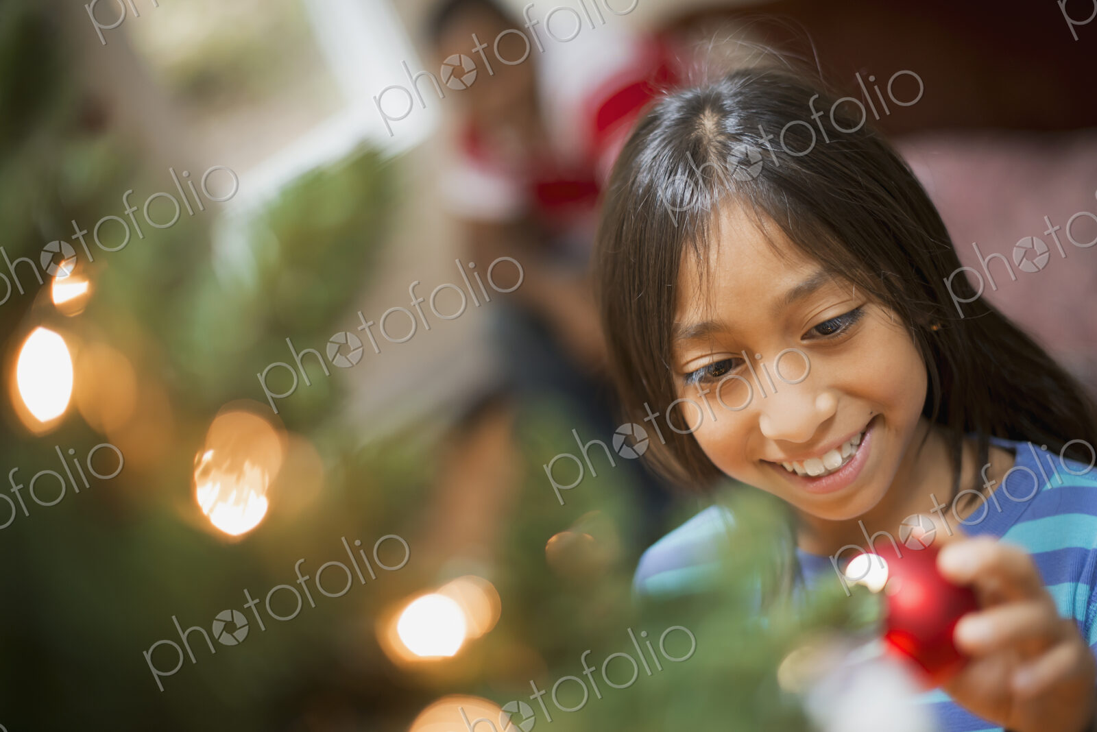 A girl placing a handmade ornament on a Christmas tree.