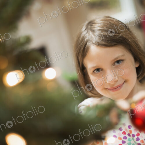 A girl placing a handmade ornament on a Christmas tree. A girl placing a handmade ornament on a Christmas tree.