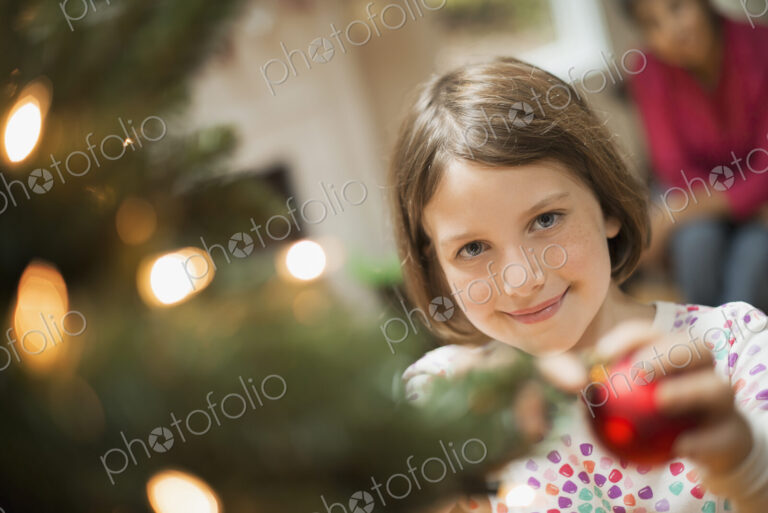 A girl placing a handmade ornament on a Christmas tree.