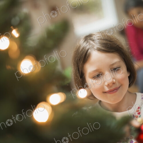 A girl placing a handmade ornament on a Christmas tree. A girl placing a handmade ornament on a Christmas tree.