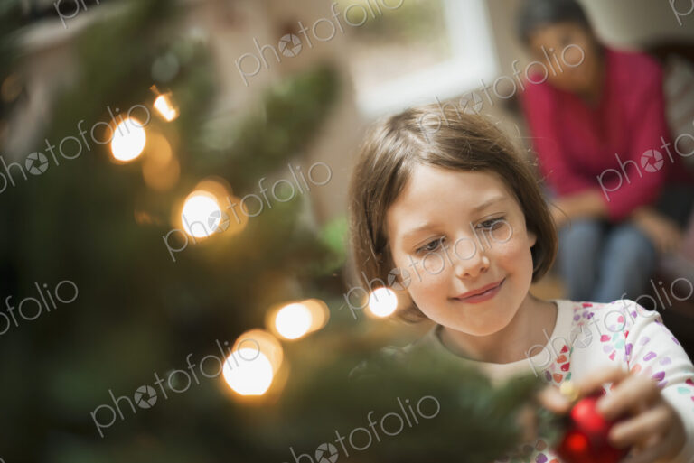 A girl placing a handmade ornament on a Christmas tree.
